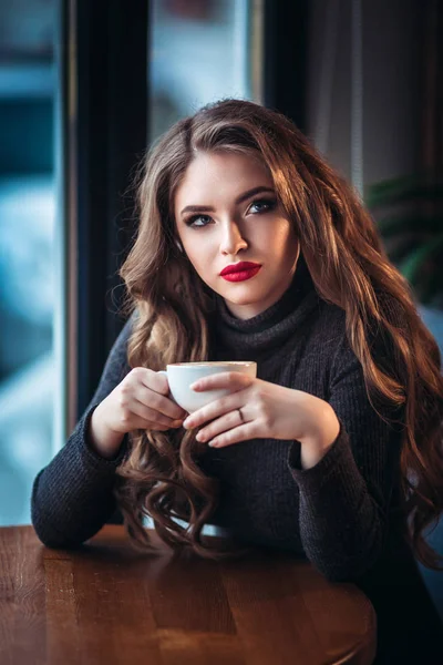 Hermosa joven mujer disfrutando de café capuchino con espuma cerca de la ventana en un café — Foto de Stock