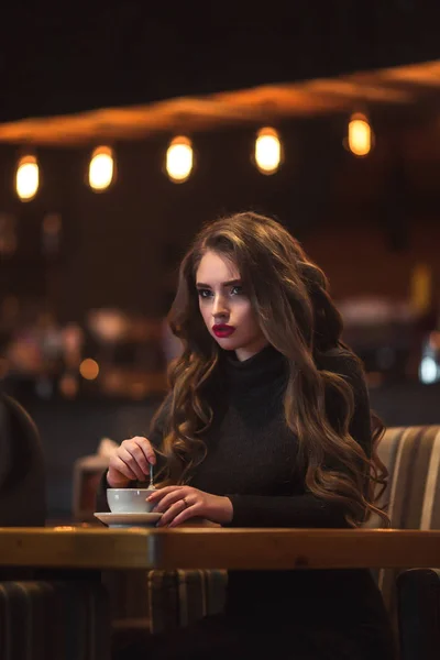 Mooie jonge vrouw genieten van koffie cappuccino met schuim in de buurt van venster in een café — Stockfoto