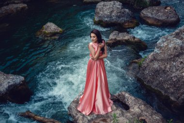 Nehir cadı. Pembe uzun elbise, muhteşem bir görüntü. Moda tonlama. Yaratıcı renk. Nehrin yanında mistik bir ormandaki güzel dansçı
