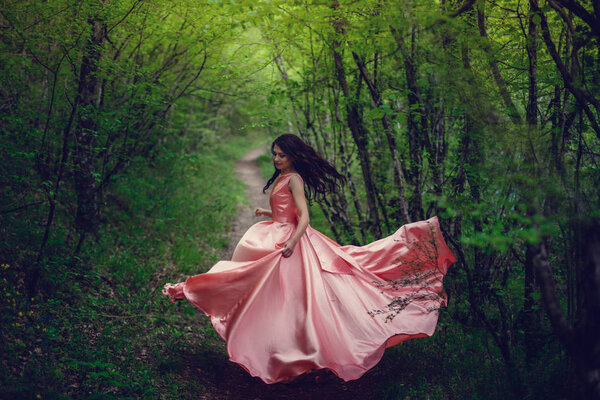 River witch. Pink long dress, a fabulous image. Fashionable toning. Creative color. Beautiful dancer in a mystical forest by the river