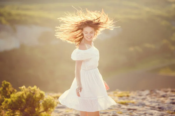 Portrait of brunette attractive woman with light smile and closed eyes for enjoy moment of walking alone in wild rocks on sunset. Girl wears white retro dress — Stock Photo, Image