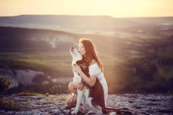 Piękna młoda kobieta, grając z zabawny pies husky na świeżym powietrzu w parku na zachód lub wschód słońca — Zdjęcie stockowe