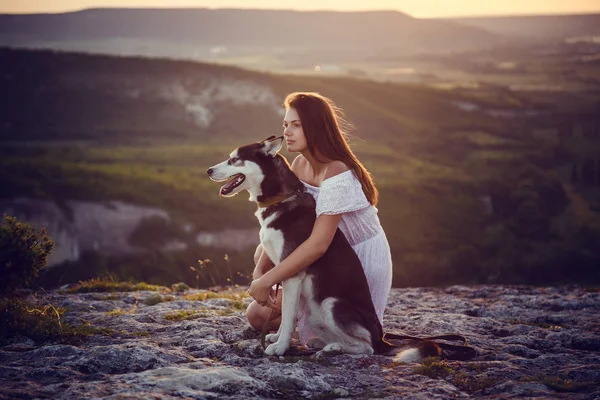 Vacker ung kvinna leker med rolig husky hund utomhus i parken vid solnedgång eller soluppgång — Stockfoto
