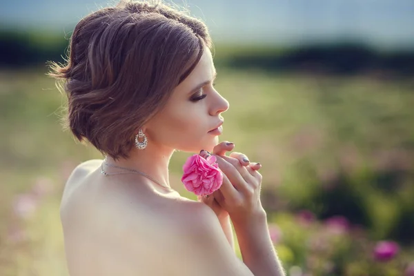 Schöne junge Frau in einem blühenden Rosengarten — Stockfoto