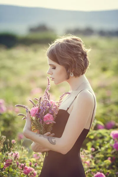 Hermosa mujer joven en un jardín de rosas en flor —  Fotos de Stock