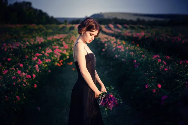 Schöne junge Frau in einem blühenden Rosengarten — Stockfoto