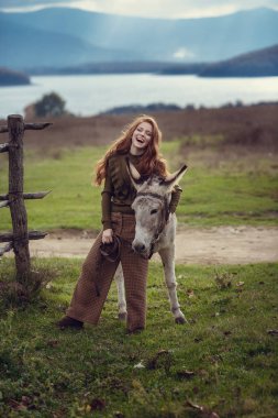 Provence tarzında modern giyimleri kıvırcık kırmızı saçlı bir kız şirin bir eşek hugs