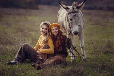 İki çekici genç kadın doğa ile birlikte bir şirin eşek üzerinde tutun.
