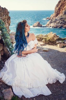 Cliff'in kenarında duran ve geniş Deniz Manzaralı arıyorum genç kadın. Rüzgar uzun mavi saç.