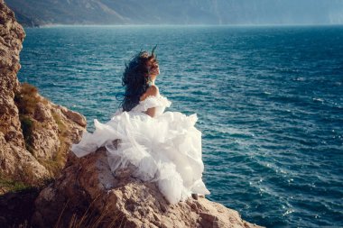 Cliff'in kenarında duran ve geniş Deniz Manzaralı arıyorum genç kadın. Rüzgar uzun mavi saç.