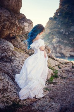 Cliff'in kenarında duran ve geniş Deniz Manzaralı arıyorum genç kadın. Rüzgar uzun mavi saç.