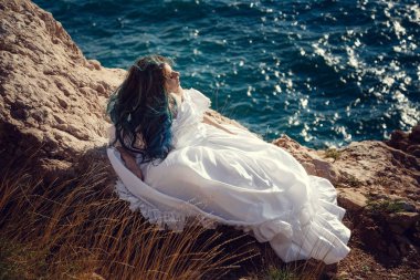 Cliff'in kenarında duran ve geniş Deniz Manzaralı arıyorum genç kadın. Rüzgar uzun mavi saç.