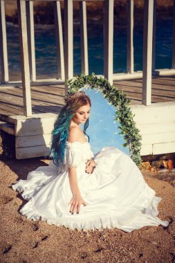 Güzel kız mavi saçlı ve beyaz vintage elbiseyle denize benziyor. Onu denizin içinde yansıtan güzel bir antika ayna eller. Kitap kapağı