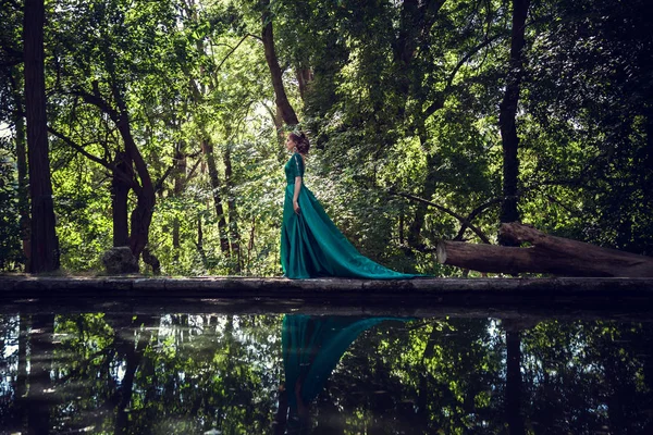 Молода жінка в зеленому платті досліджує чарівний ліс — стокове фото