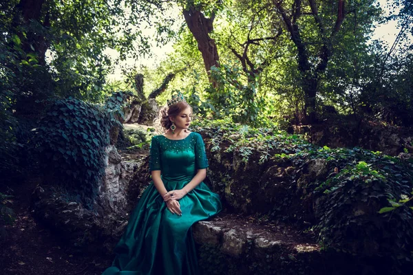 Ung kvinna som bär en grön klänning utforskar en magisk skog — Stockfoto