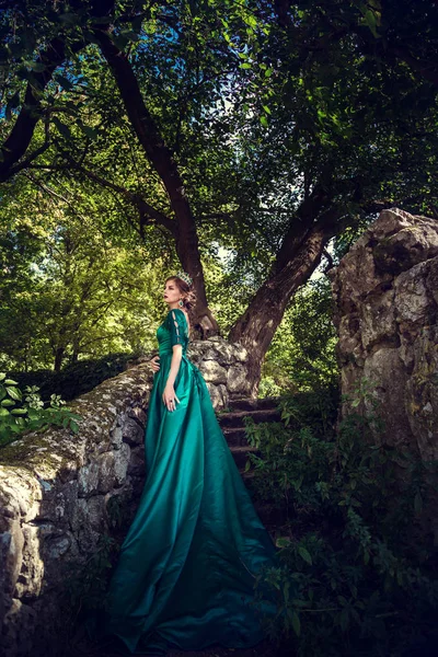 Ung kvinna som bär en grön klänning utforskar en magisk skog — Stockfoto
