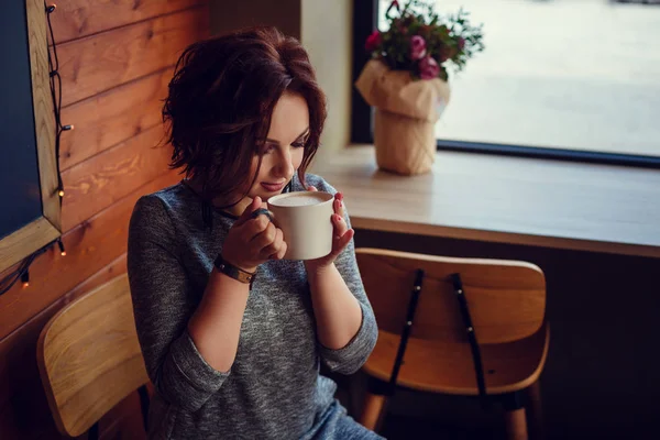 Linda mujer bebiendo café en taza blanca en café en la ciudad. Moda casual de otoño, aspecto elegante todos los días. Modelo de tamaño más . — Foto de Stock