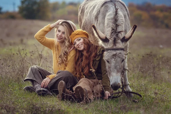 Twee charmante jonge vrouwen rusten op de natuur samen met een schattig ezel. — Stockfoto