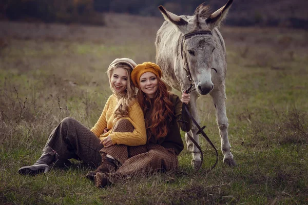 Twee charmante jonge vrouwen rusten op de natuur samen met een schattig ezel. — Stockfoto