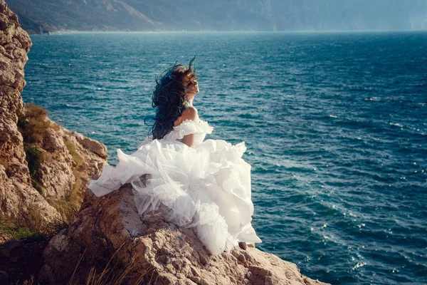 Cliff'in kenarında duran ve geniş Deniz Manzaralı arıyorum genç kadın. Rüzgar uzun mavi saç.