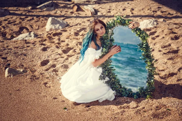 海で美少女青い髪と白いヴィンテージのドレスに見えます。彼女の手の海が反映して美しいアンティーク ミラーを実行します。本の表紙 — ストック写真