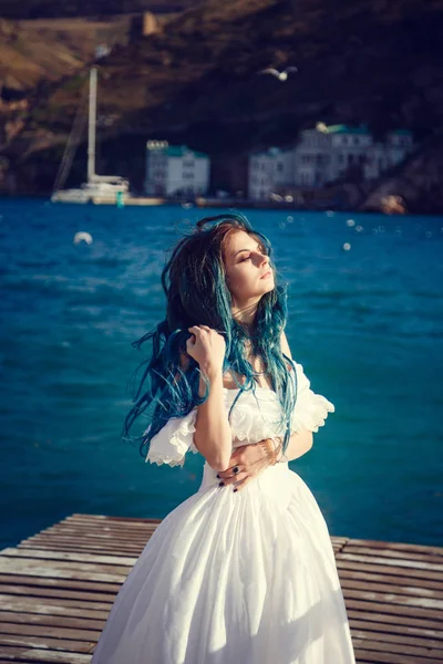 Bella ragazza con i capelli blu e in un abito bianco vintage guarda il mare, il vento gioca nei suoi capelli . — Foto Stock