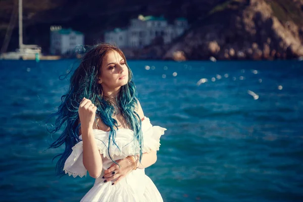 Schöne Mädchen mit blauen Haaren und in einem weißen Vintage-Kleid blickt auf das Meer, der Wind spielt in ihren Haaren. — Stockfoto