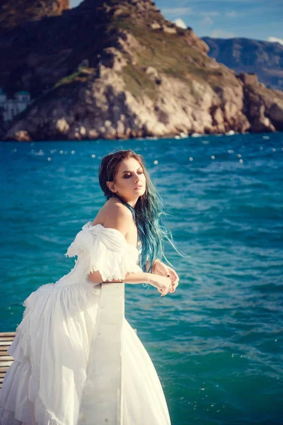 Schöne Mädchen mit blauen Haaren und in einem weißen Vintage-Kleid blickt auf das Meer, der Wind spielt in ihren Haaren. — Stockfoto