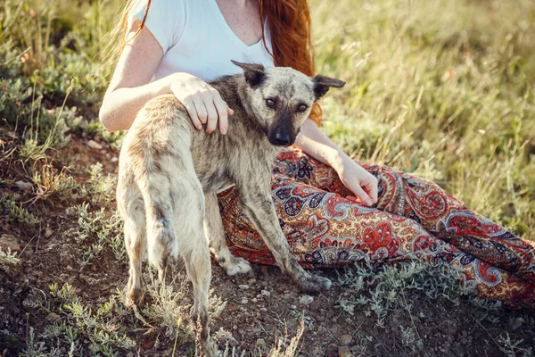 Ein junges Mädchen im Boho-Stil, an der Küste mit ihrem Hund. Idee und Konzept von Freiheit und Hippies — Stockfoto