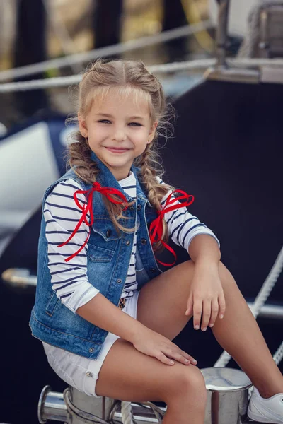 Una bellissima bambina in stile marino sullo sfondo di barche e yacht. Piccolo marinaio — Foto Stock