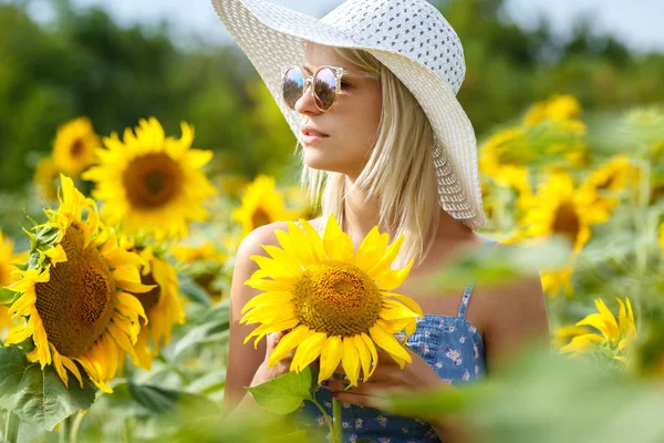 Schöne junge Frau mit Hut und Brille auf einem Sonnenblumenfeld — Stockfoto