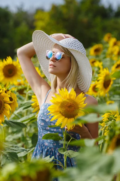 Schöne junge Frau mit Hut und Brille auf einem Sonnenblumenfeld — Stockfoto