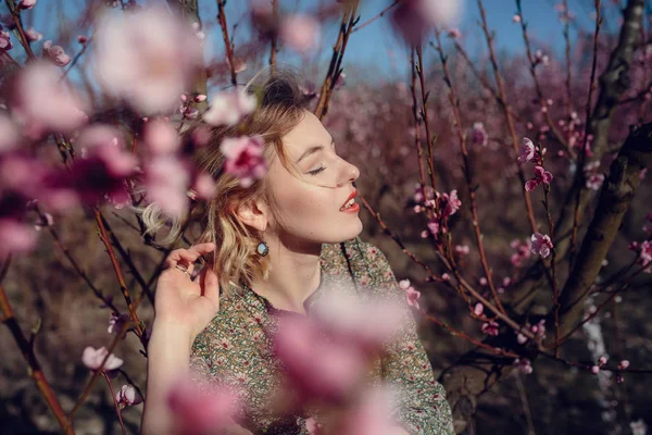 Fashion outdoor photo of gorgeous young woman in elegant dress posing in garden with blossom peach trees — Stock Photo, Image