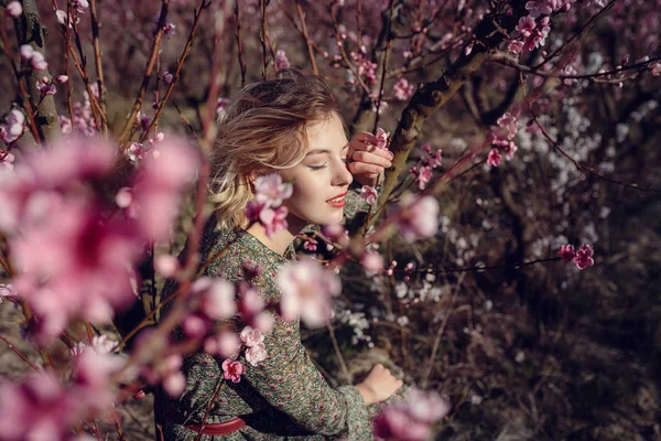 Fashion outdoor photo of gorgeous young woman in elegant dress posing in garden with blossom peach trees — Stock Photo, Image
