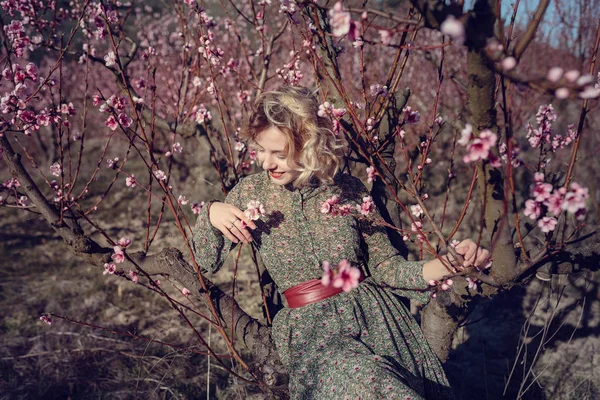 Fashion outdoor photo of gorgeous young woman in elegant dress posing in garden with blossom peach trees — Stock Photo, Image