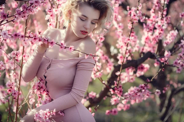 Moda foto ao ar livre de linda jovem mulher em vestido elegante posando no jardim com árvores de pêssego flor — Fotografia de Stock