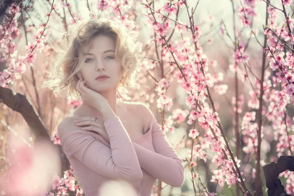 Foto de moda al aire libre de la hermosa mujer joven en vestido elegante posando en el jardín con árboles de melocotón en flor —  Fotos de Stock