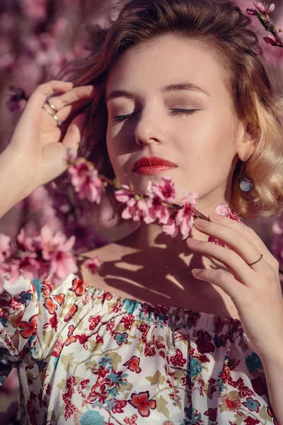 Mode buiten foto van prachtige jonge vrouw in elegante jurk poseren in de tuin met perzik bloesem bomen — Stockfoto