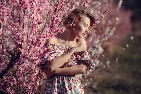 Mode utomhus foto av vackra unga kvinna i elegant klänning poserar i trädgården med blossom persika träd — Stockfoto