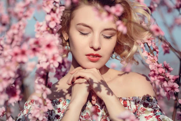 Mode buiten foto van prachtige jonge vrouw in elegante jurk poseren in de tuin met perzik bloesem bomen — Stockfoto