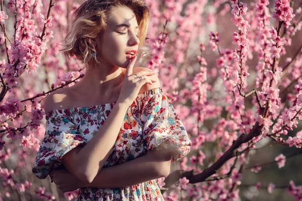 Módní venkovní foto nádherné mladé ženy v elegantních šatech pózuje v zahradě se stromy květ broskve — Stock fotografie