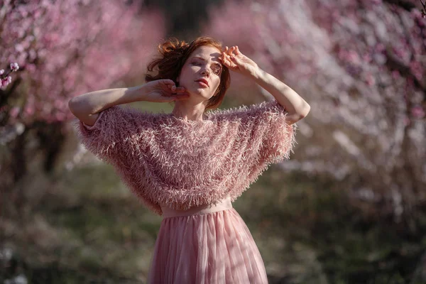 Piękna młoda dziewczyna z rude włosy w delikatny brzoskwiniowy ogród, który rozkwitł. — Zdjęcie stockowe