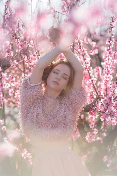 Vacker ung flicka med rött hår i en mild persika trädgård, som blommade. — Stockfoto