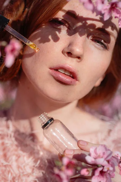 Beautiful young girl with red hair in a gentle peach garden, which blossomed.