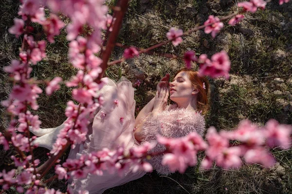 Hermosa joven con el pelo rojo en un jardín de melocotón suave, que floreció . — Foto de Stock