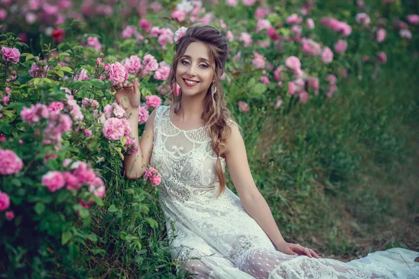 Bella donna in un parco floreale, rose da giardino. Trucco, capelli, una corona di rose . — Foto Stock
