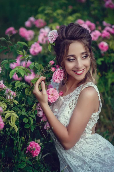 Vacker kvinna i en blomsterpark, trädgård rosor. Makeup, hår, en krans av rosor. — Stockfoto