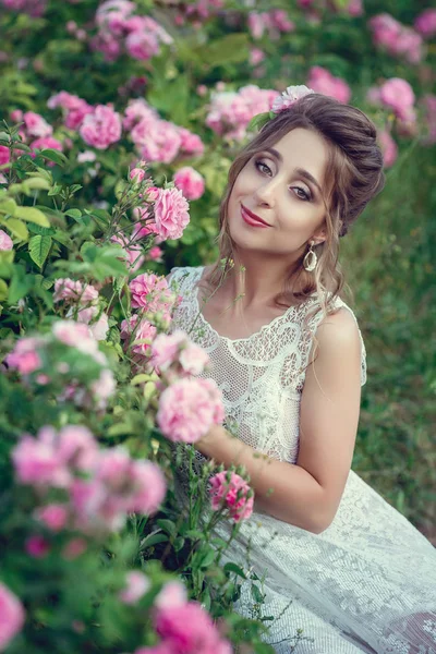 Vacker kvinna i en blomsterpark, trädgård rosor. Makeup, hår, en krans av rosor. — Stockfoto