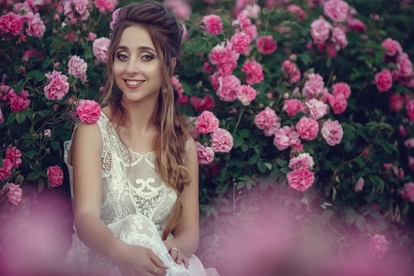 Vacker kvinna i en blomsterpark, trädgård rosor. Makeup, hår, en krans av rosor. — Stockfoto