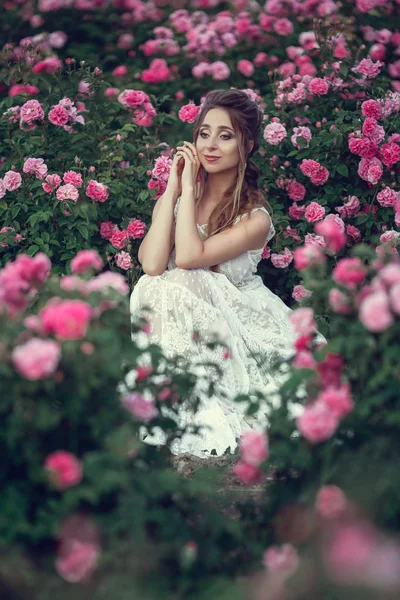 Bella donna in un parco floreale, rose da giardino. Trucco, capelli, una corona di rose . — Foto Stock